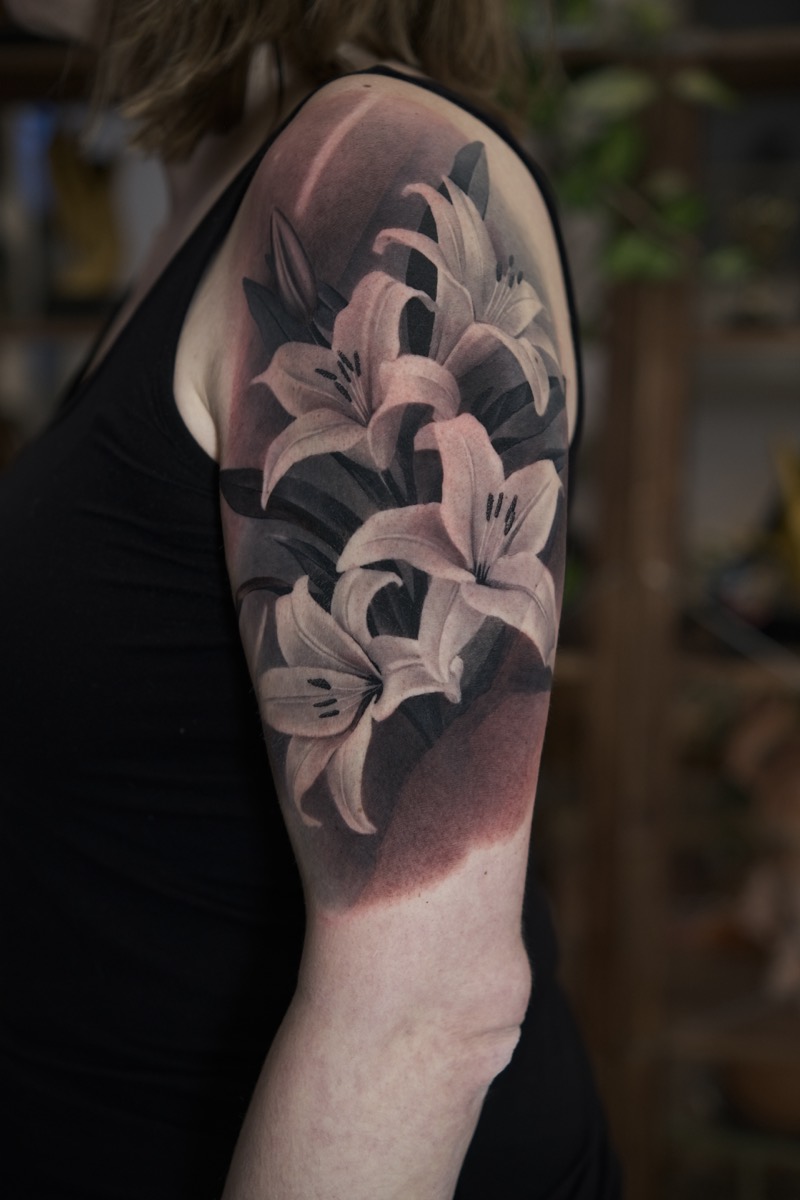 Black & Grey Tattoo an Schulter und Oberarm: mehrere Lilienblüten mit weichen Schattierungen