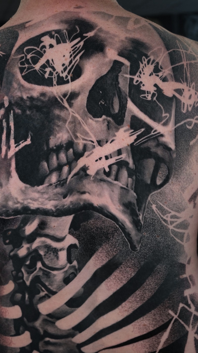 Nahaufnahme des Rücken-Tattoos: Schädel mit hellen Kritzel-Akzenten, Dotwork-Schattierung und Wirbelsäule